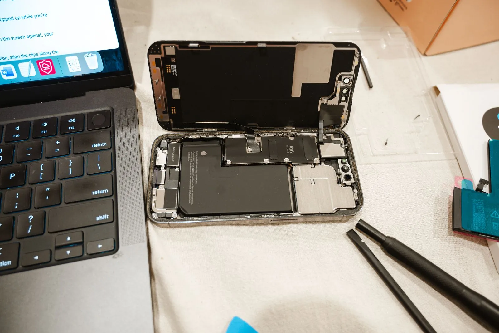 Otvorený iPhone s viditeľnou batériou vedľa servisného náradia